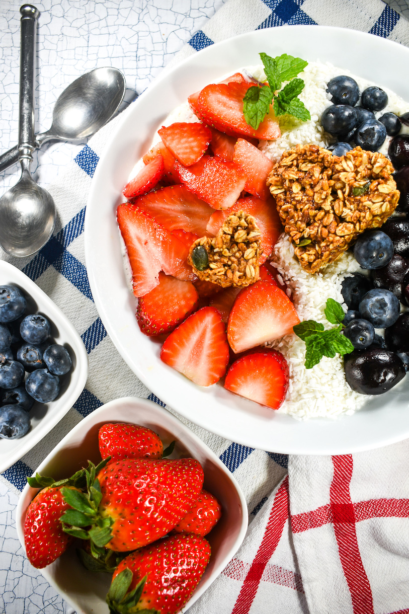Smoothie bowl on a plaid tea towel, along with bowls of strawberries and blueberries