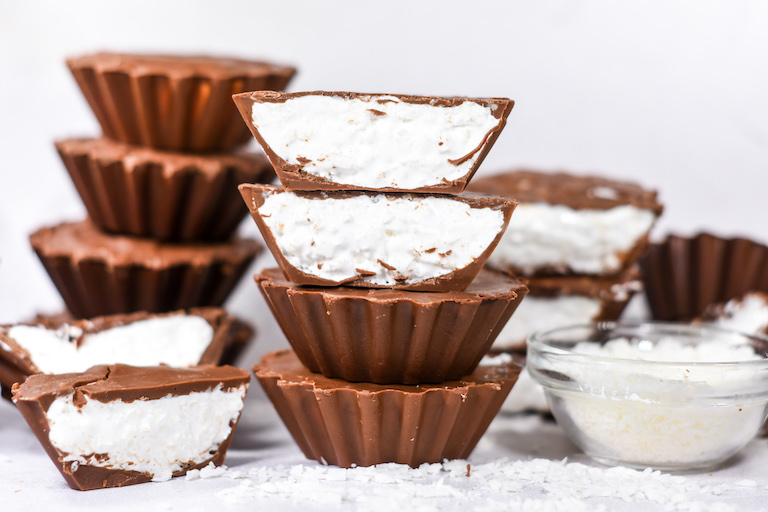 Stacks of homemade Mallo Cups and a bowl of coconut on a white surface