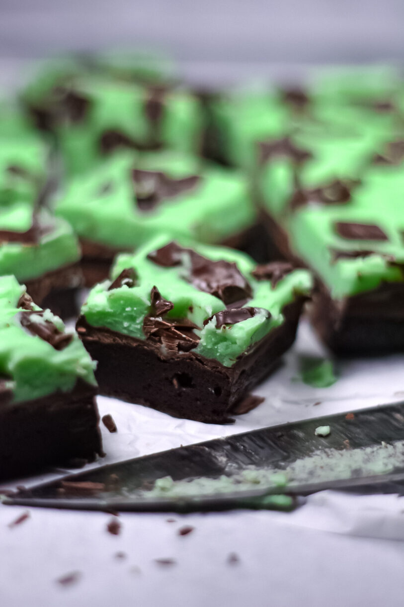 Brownies with mint icing and a knife on a white surface
