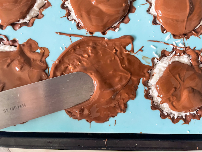 Palette knife smoothing chocolate on top of homemade coconut marshmallow cups