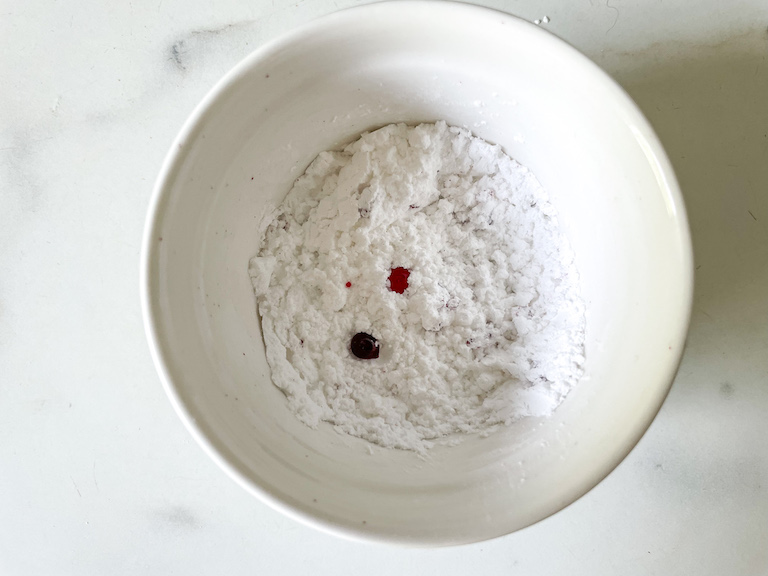 Food coloring and confectioner's sugar in a small white bowl