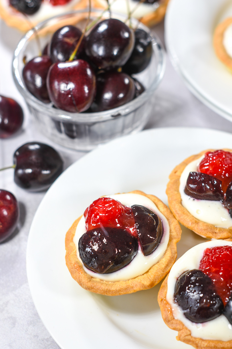 Mini berry tarts on a plate, and a glass bowl of cherries