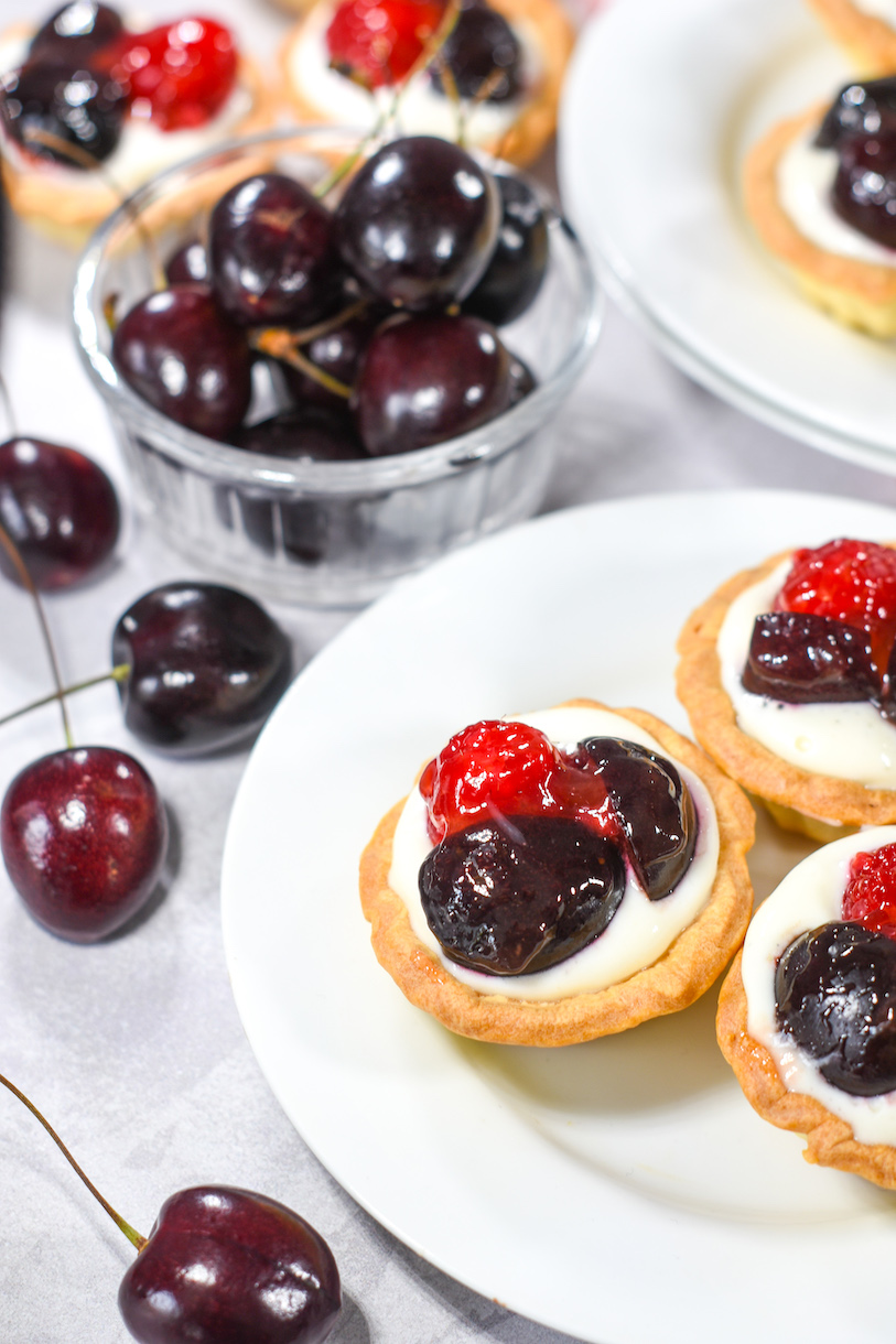 Raspberry tartlets and a bowl of cherries on a white surface