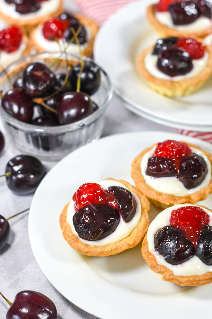 Mini berry cherry tartlets, white plates, and a bowl of cherries