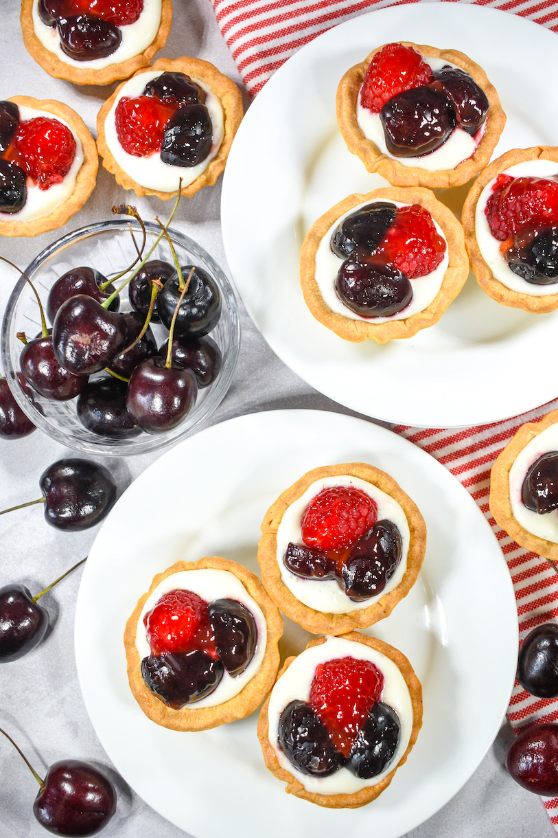 Two plates of mini tarts, a red striped towel, and fresh cherries