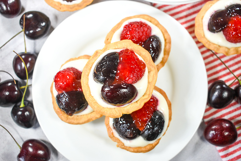 A plate of cherry and raspberry tarts, surrounded by cherries