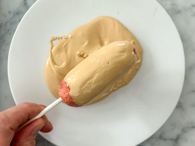 Hand dipping a cake pop in melted chocolate