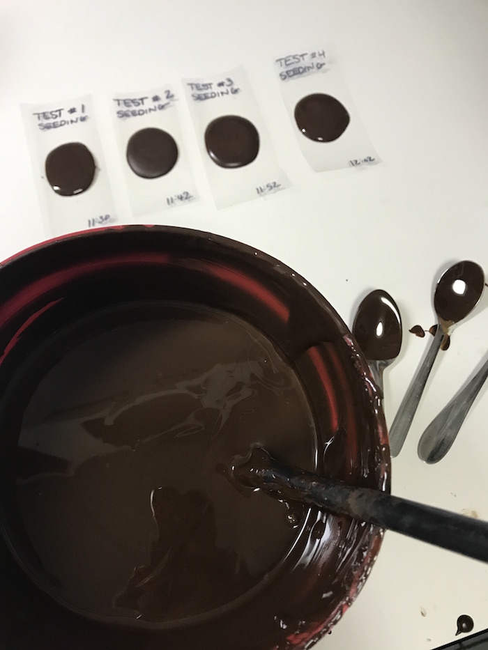 A bowl of chocolate and tempering tests on parchment
