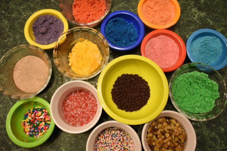 Colored sugars, sprinkles, and nuts in small bowls on a countertop