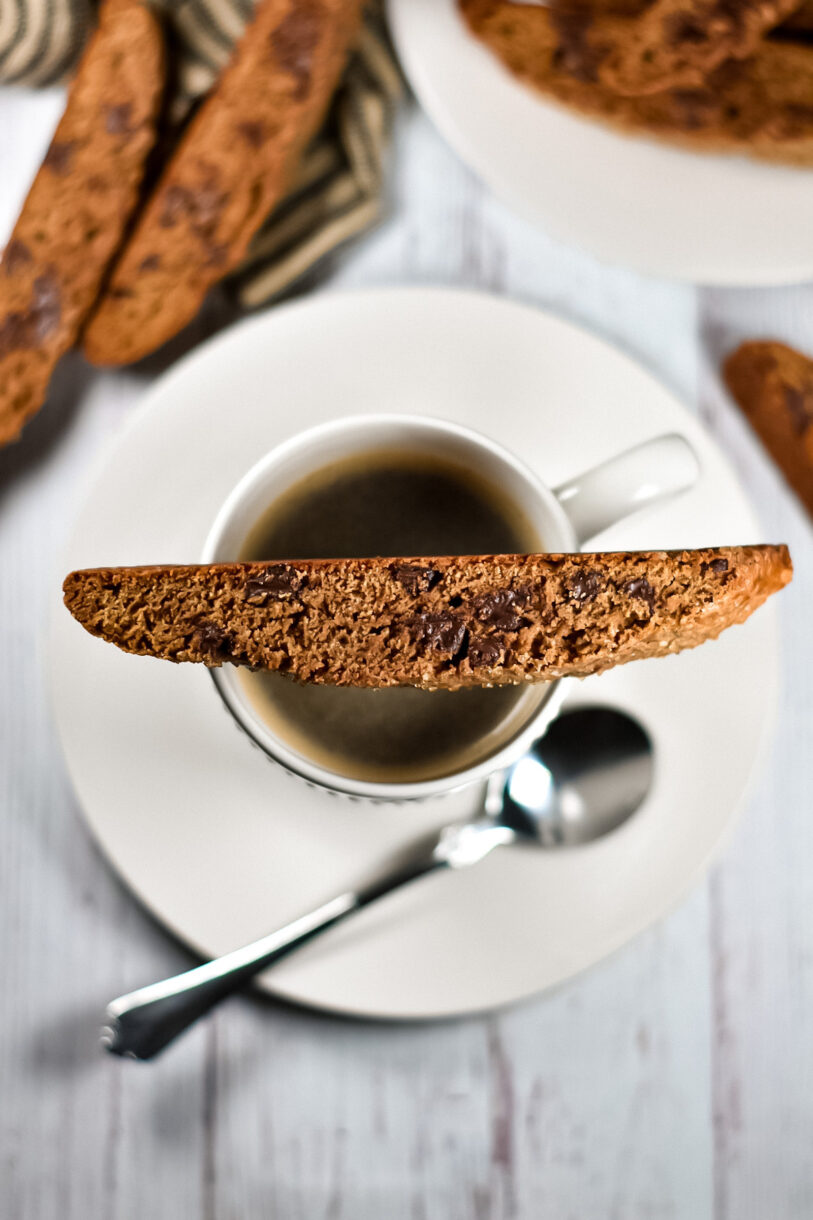 Chocolate Espresso Biscotti cookie balanced on a white mug filled with coffee