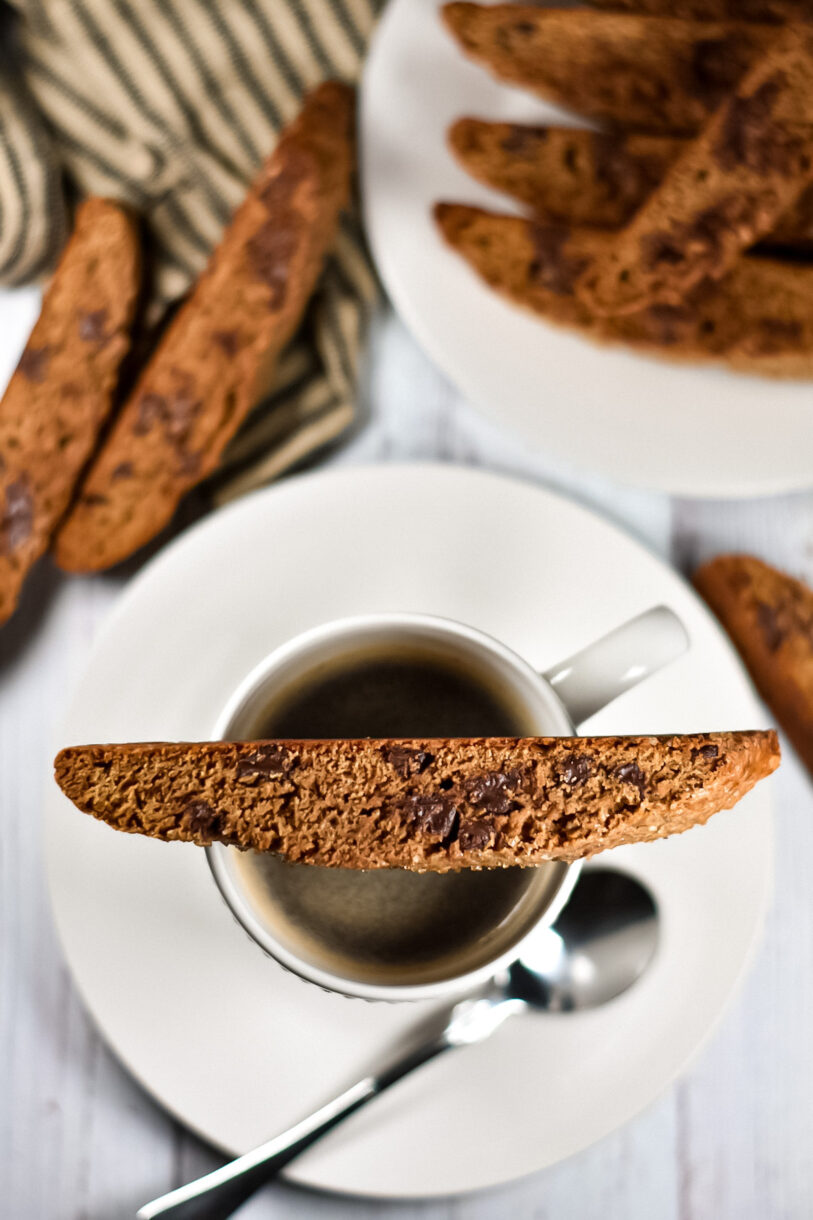 Chocolate Espresso Biscotti balanced on a cup of coffee, with saucer and spoon underneath