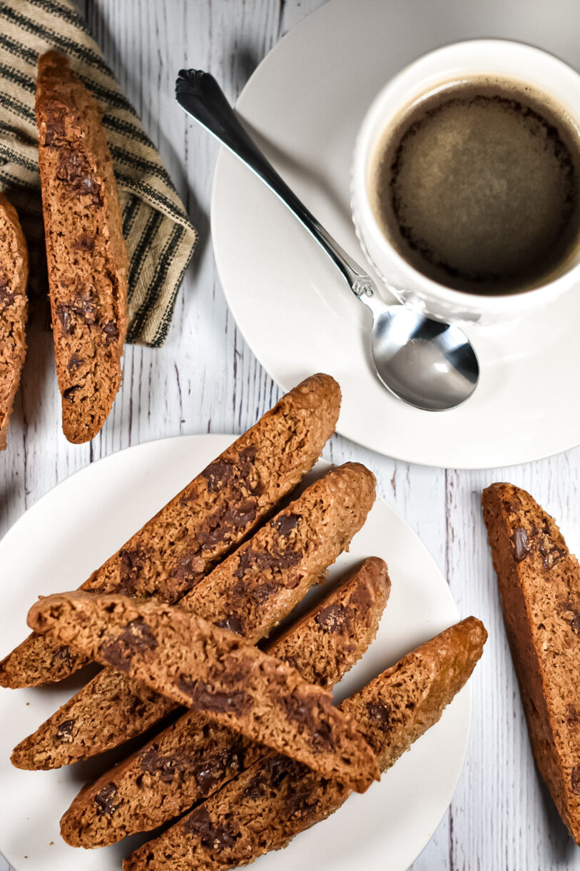 Espresso Chocolate Chip Biscotti on a white plate, a cup of coffee, and a tea towel 