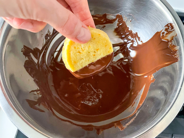Hand dipping a cookie in dark chocolate