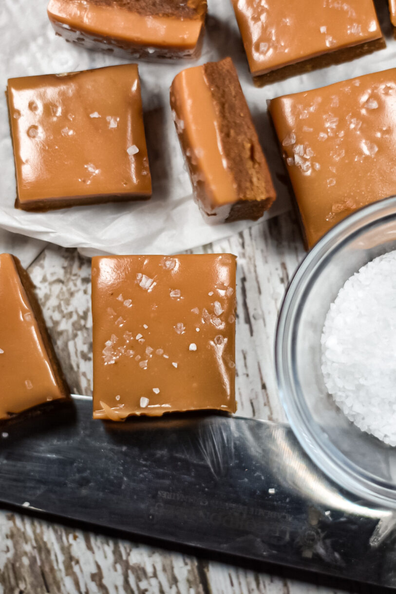 Salted Caramel Blondies, a knife, and dish of sea salt on white surface