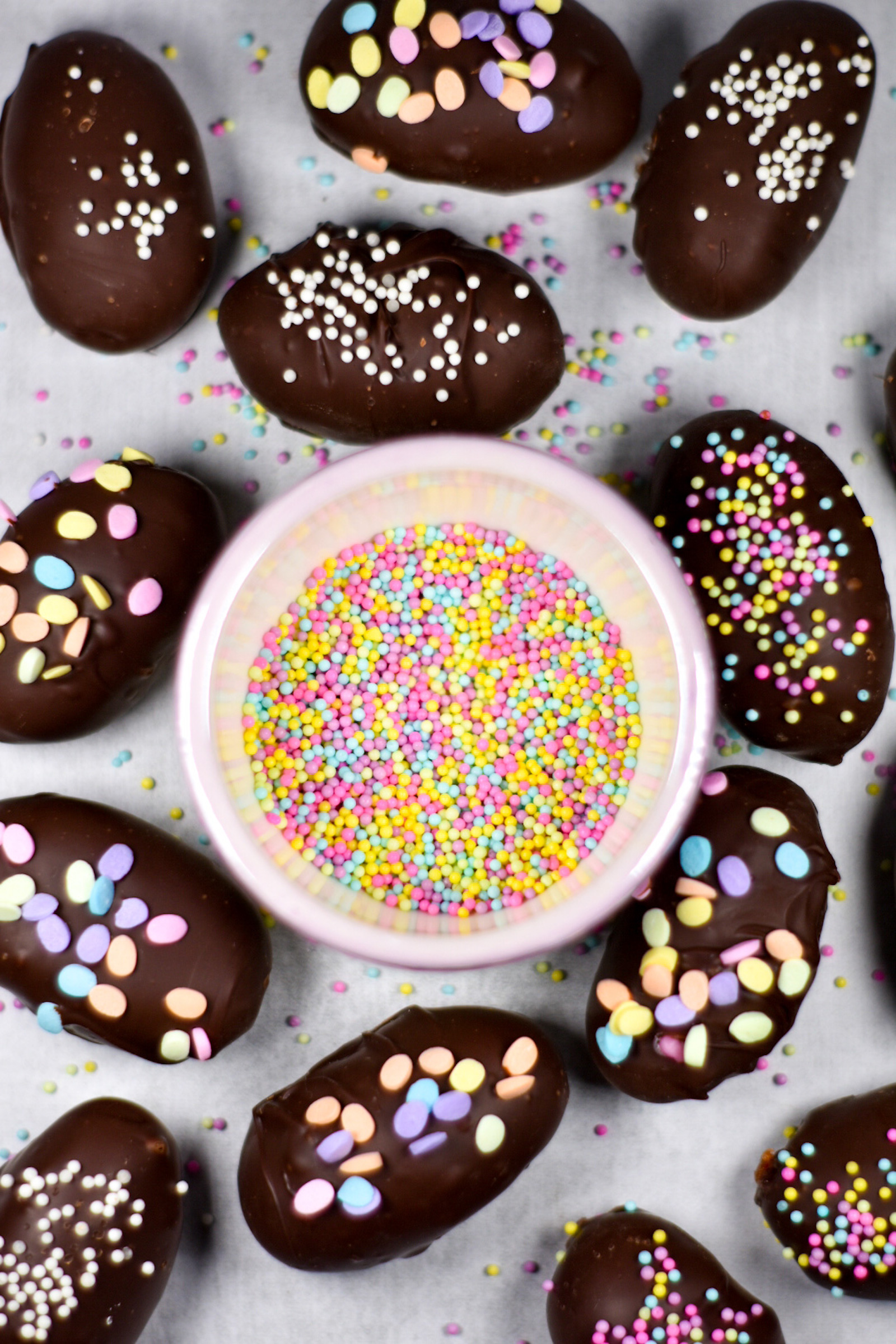 chocolate Easter eggs surrounding a bowl of pastel sprinkles