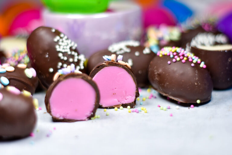 Pink buttercream Easter eggs and chocolate eggs on a white surface with sprinkles