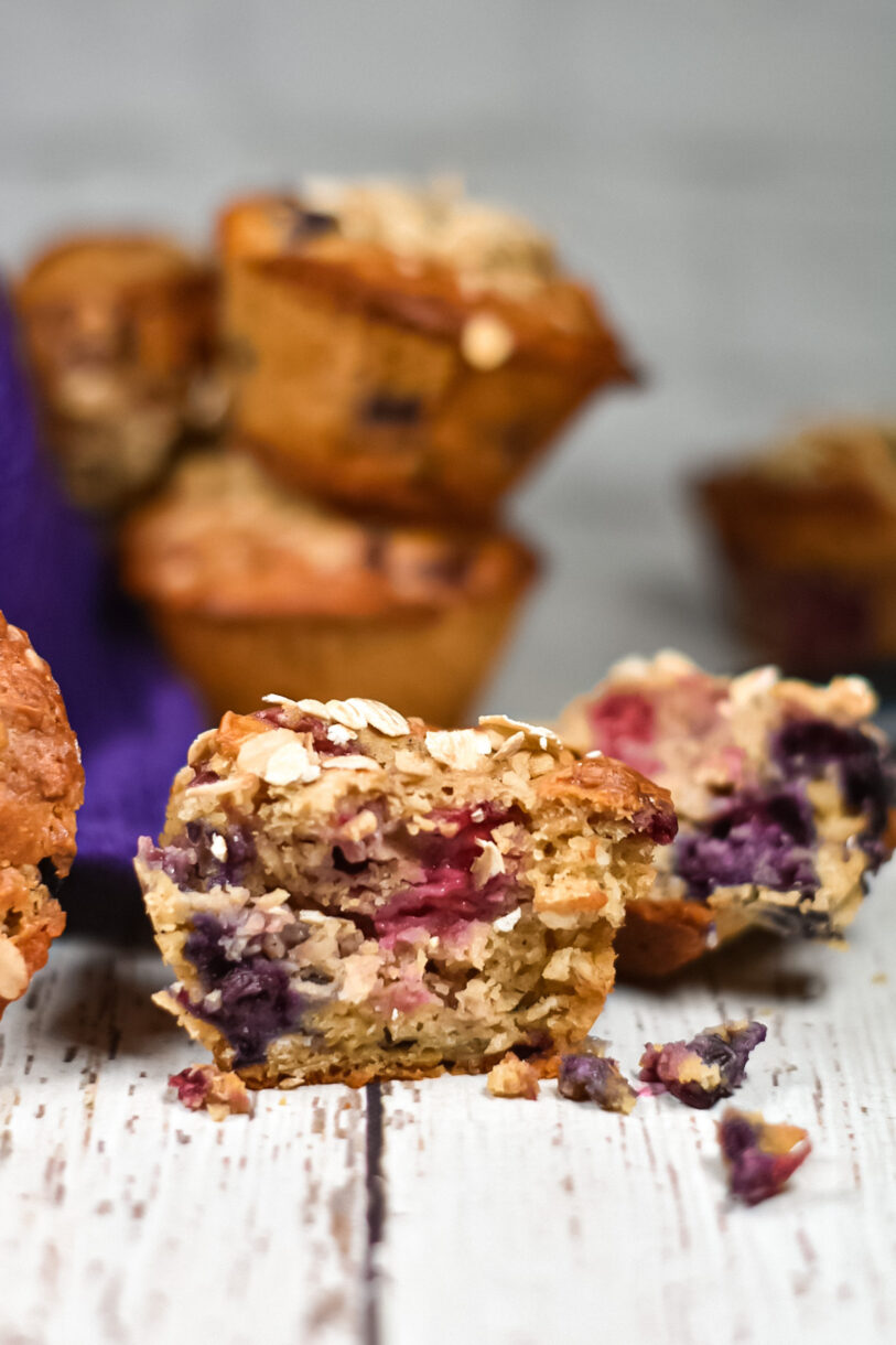 Mixed berry oatmeal cornmeal muffins, half-eaten, on a white wood surface