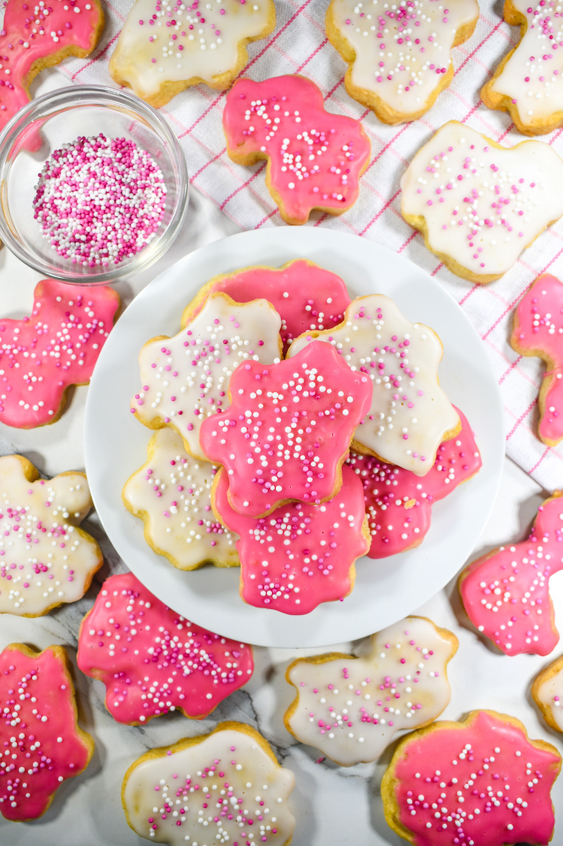Animal crackers with icing, arranged on a plate next to a tea towel and bowl of sprinkles