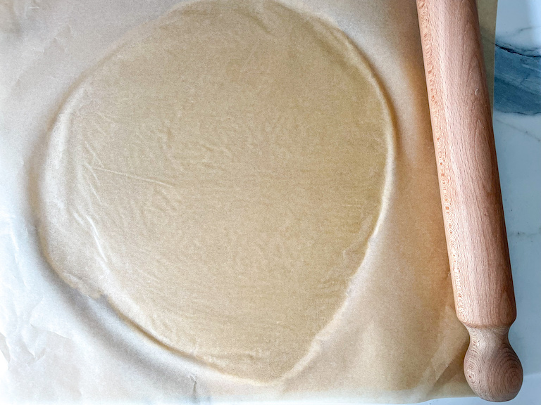 Rolling pin next to rolled dough between sheets of parchment