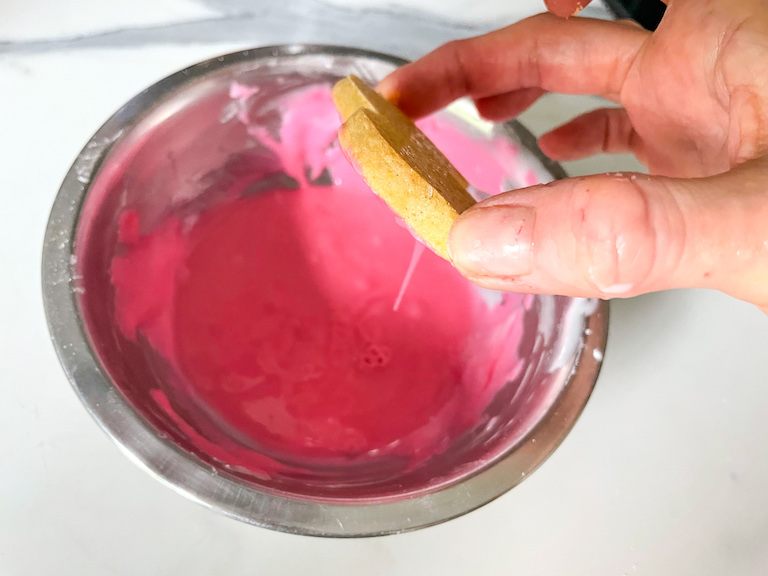 Hand dipping an animal cookie in pink frosting