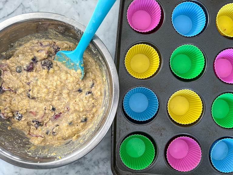 A muffin tin with silicone liners next to a bowl of muffin batter