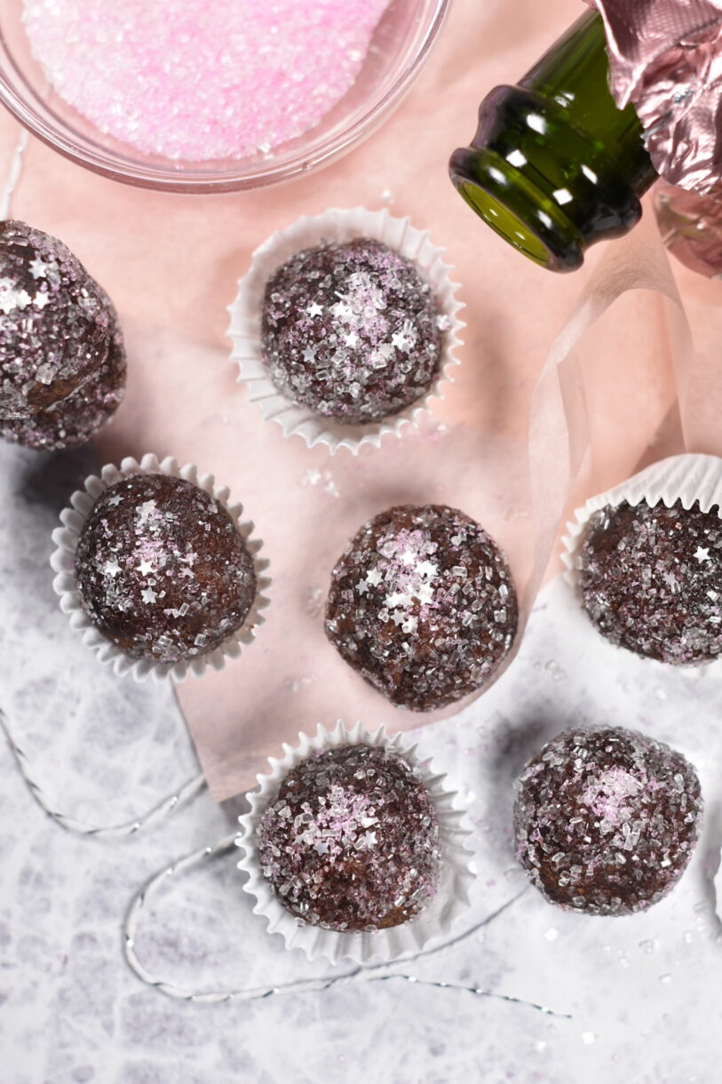 Sparkling Rosé Truffles decorated with pink sugar and edible foil stars, in white truffle cups on white textured surface