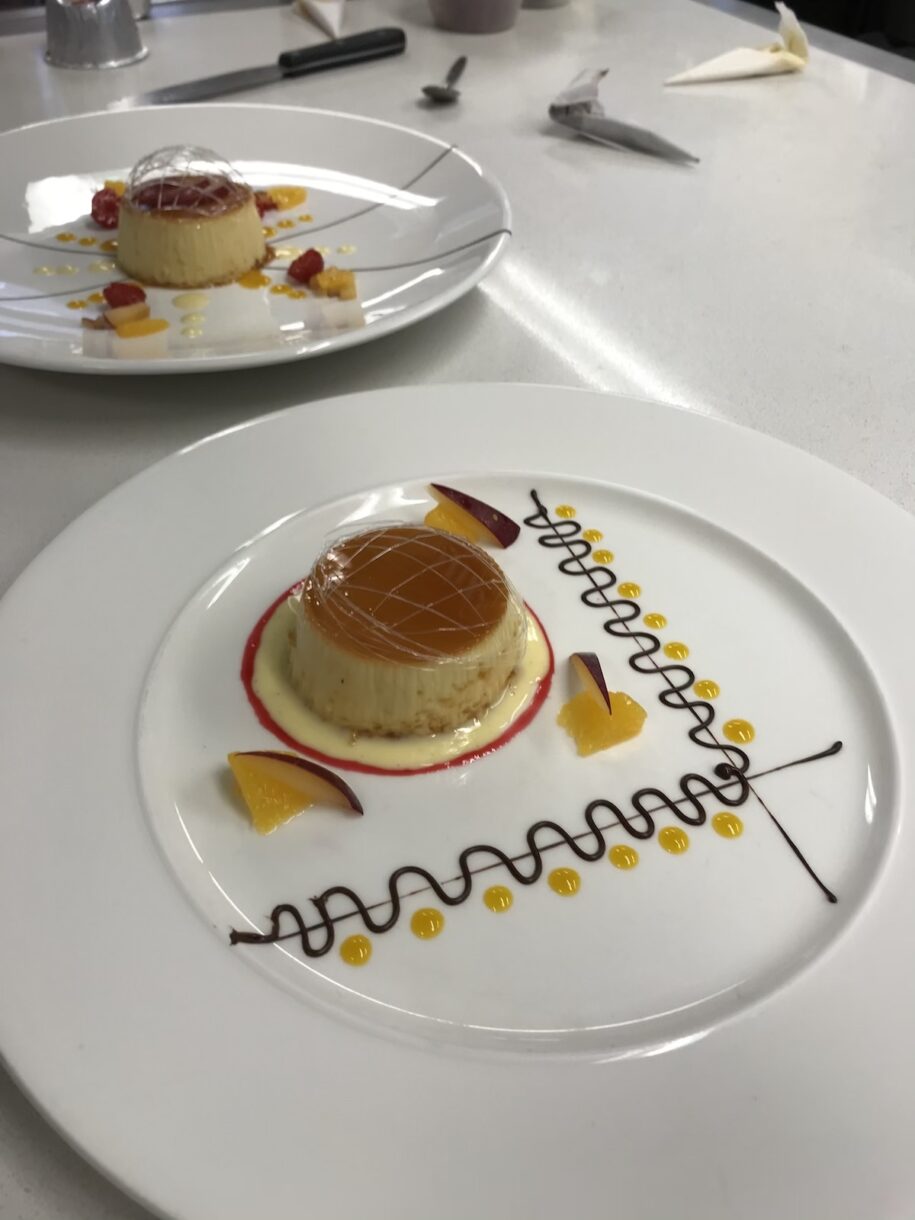 Chef's demo of creme caramel, plated on white plates with chocolate piping and fruit coulis