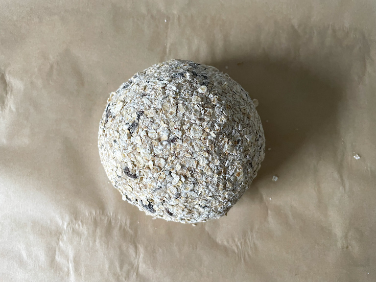 Oat coated ball of bread dough on a sheet of parchment