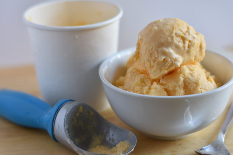A dish of homemade mango ice cream and an ice cream scoop