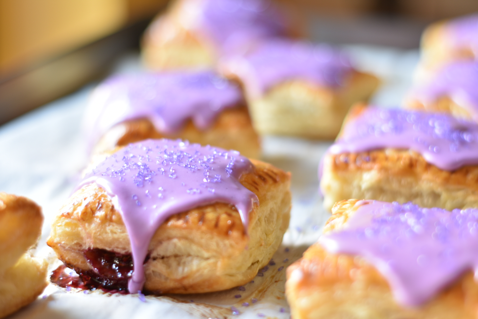 puff pastry hand pies with purple frosting on a white surface