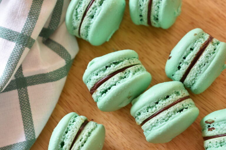 Chocolate filled macs with green shells, next to a tea towel on a wood surface