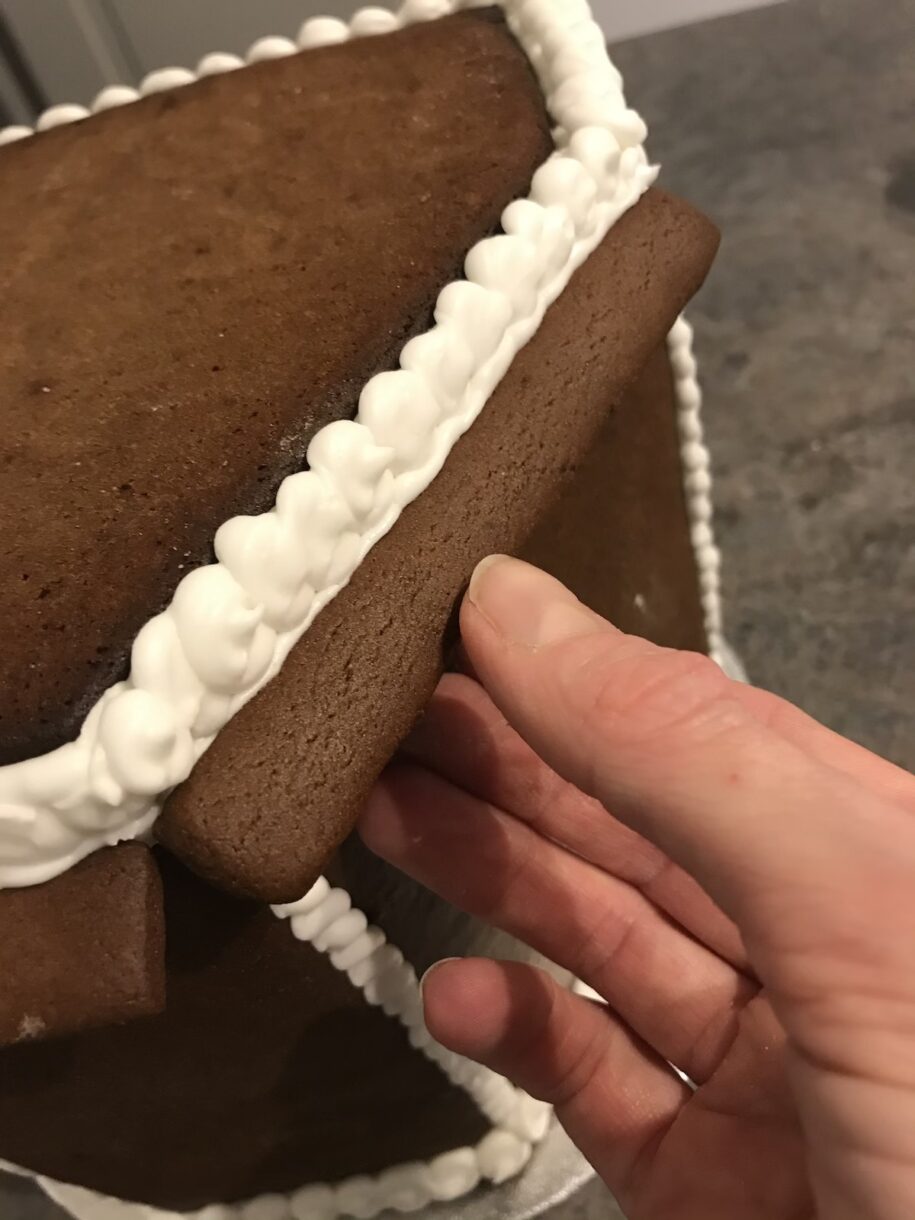 Hand attaching pieces to a gingerbread house