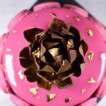 Bright pink entremet decorated with macarons and gold chocolate rose