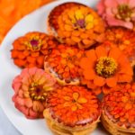 A plate of hand painted floral macarons in orange and red tones