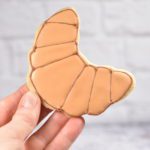 Hand holding a croissant shaped royal icing cookie