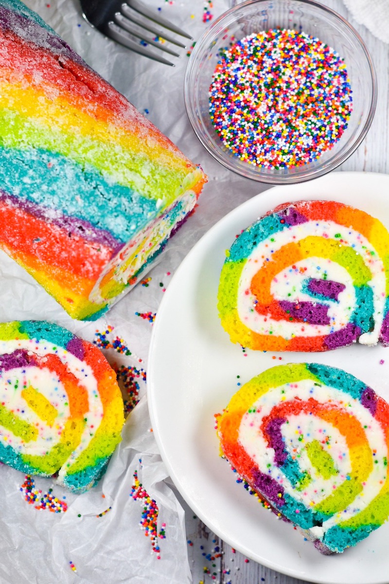 A rainbow cake roll on a white surface with rainbow sprinkles - Baste Cut Fold frequently asked questions page