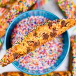 A chocolate chip biscotti cookie sitting on a bowl of sprinkles