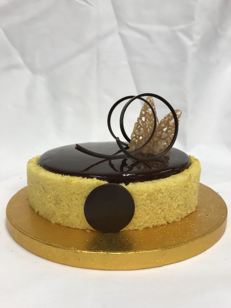 Entremet on a gold board, with yellow sponge wrap, chocolate glacage, and tempered chocolate decoration