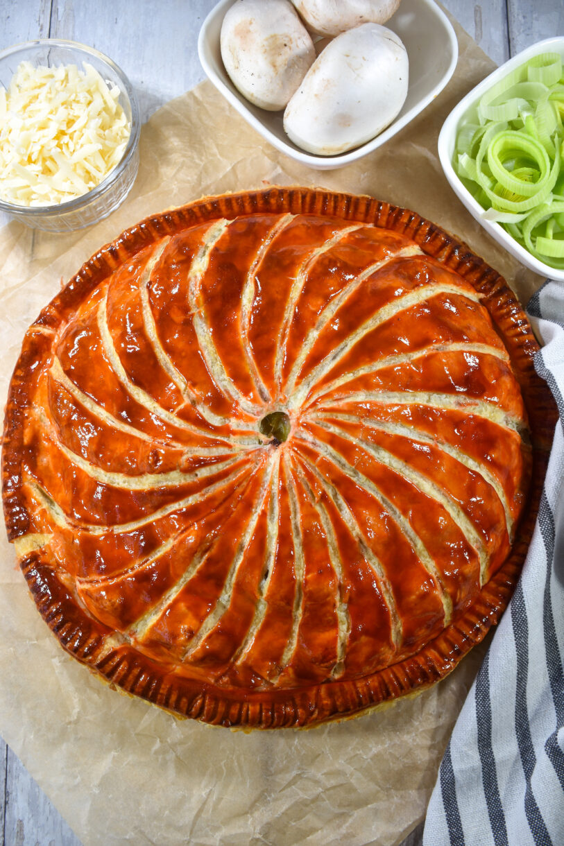 Pithivier on a sheet of parchment with leeks, mushrooms, and grated cheese