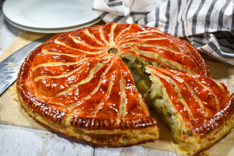 Pithivier with a slice cut out of it, and plates and towel in the background