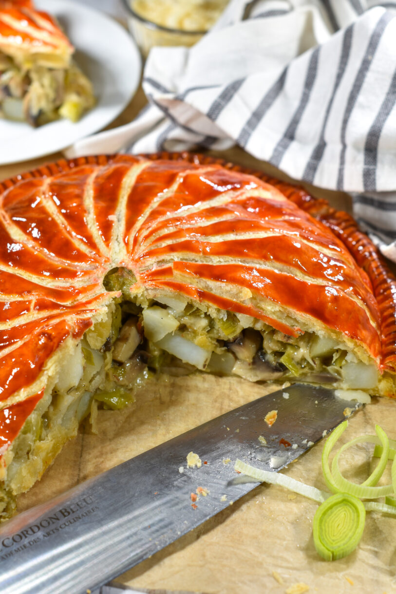 Pithivier with slice missing, accompanied by leeks and knife