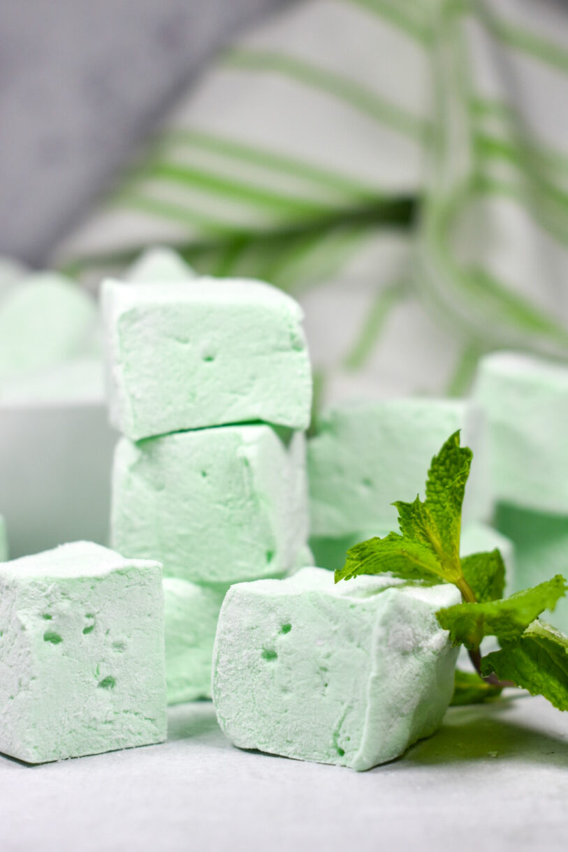 Stack of green pepperint marshmallows made from this peppermint marshmallow recipe, alongside fresh mint leaves