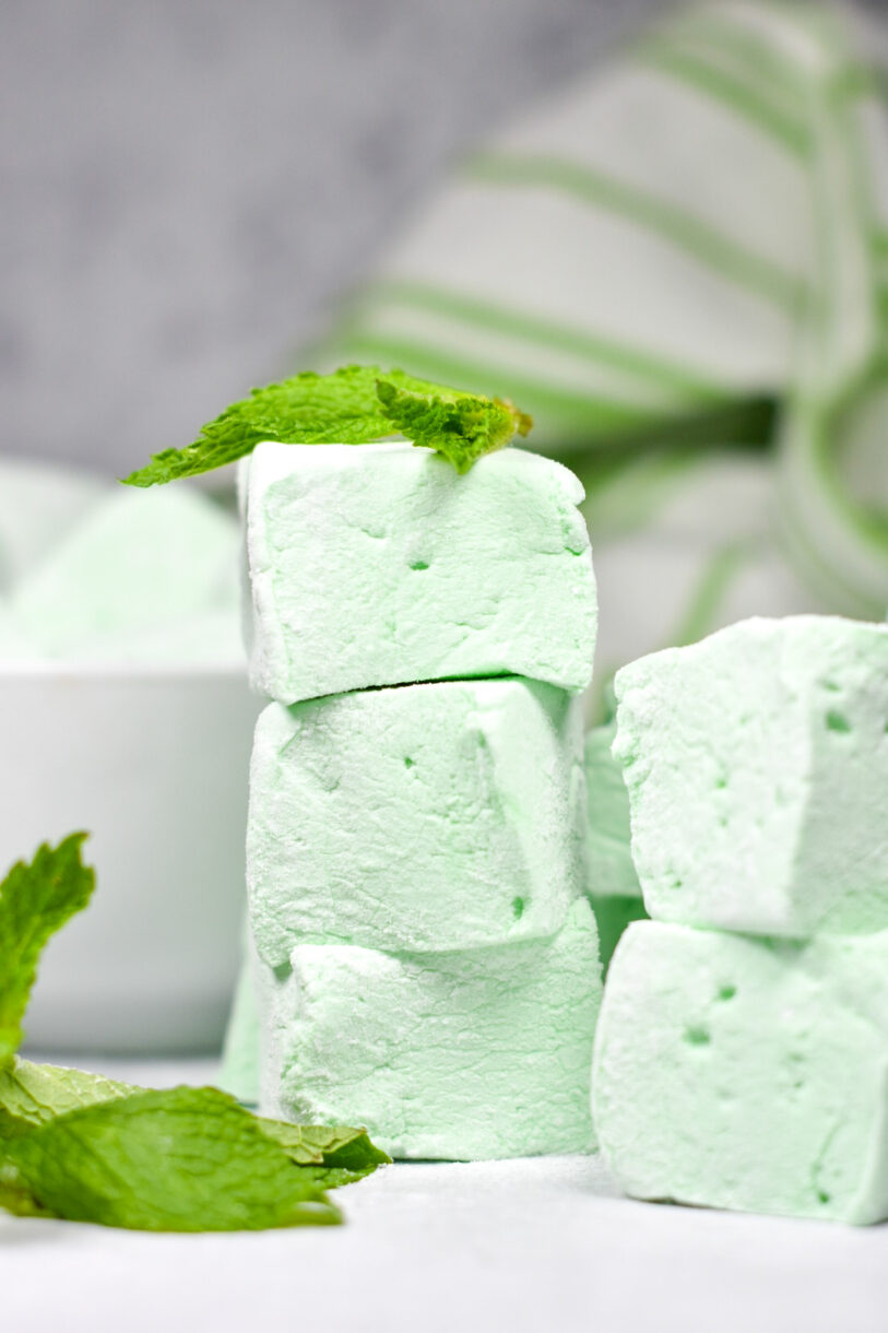Stack of marshmallows with sprig of mint on top, with green striped tea towel, made from this peppermint marshmallow recipe