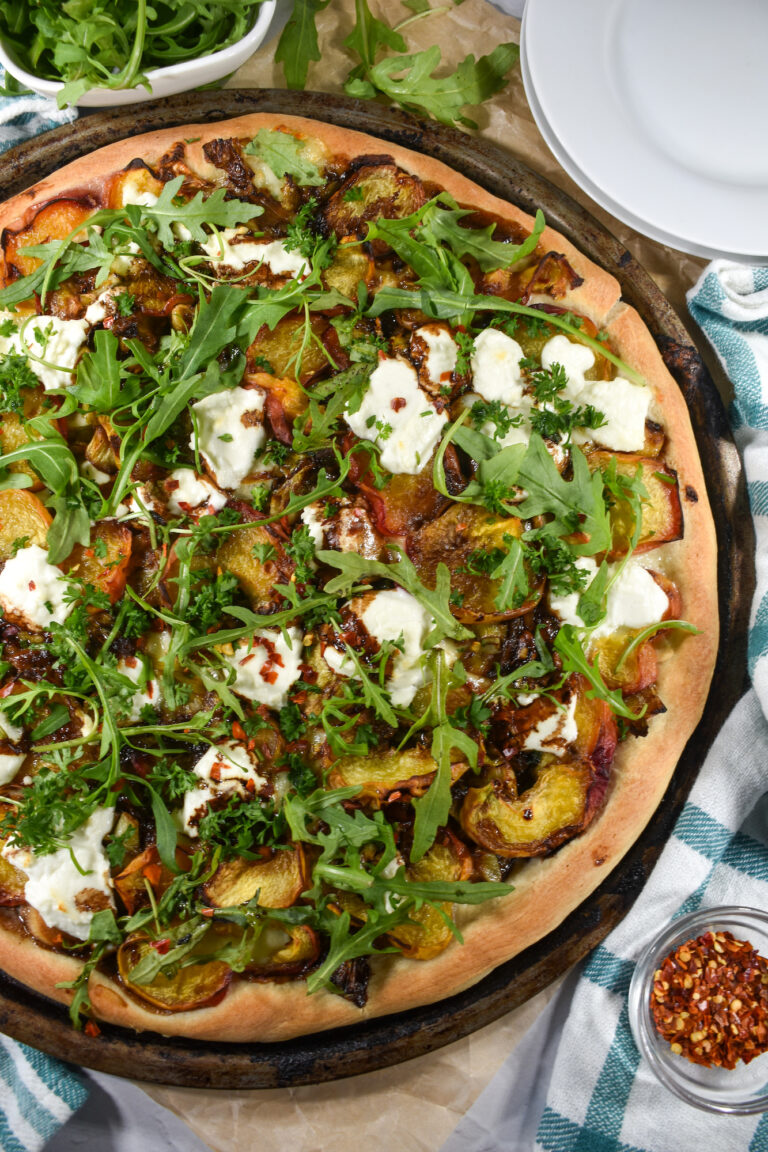 A pizza with peaches, goat cheese, mozzarella, and arugula