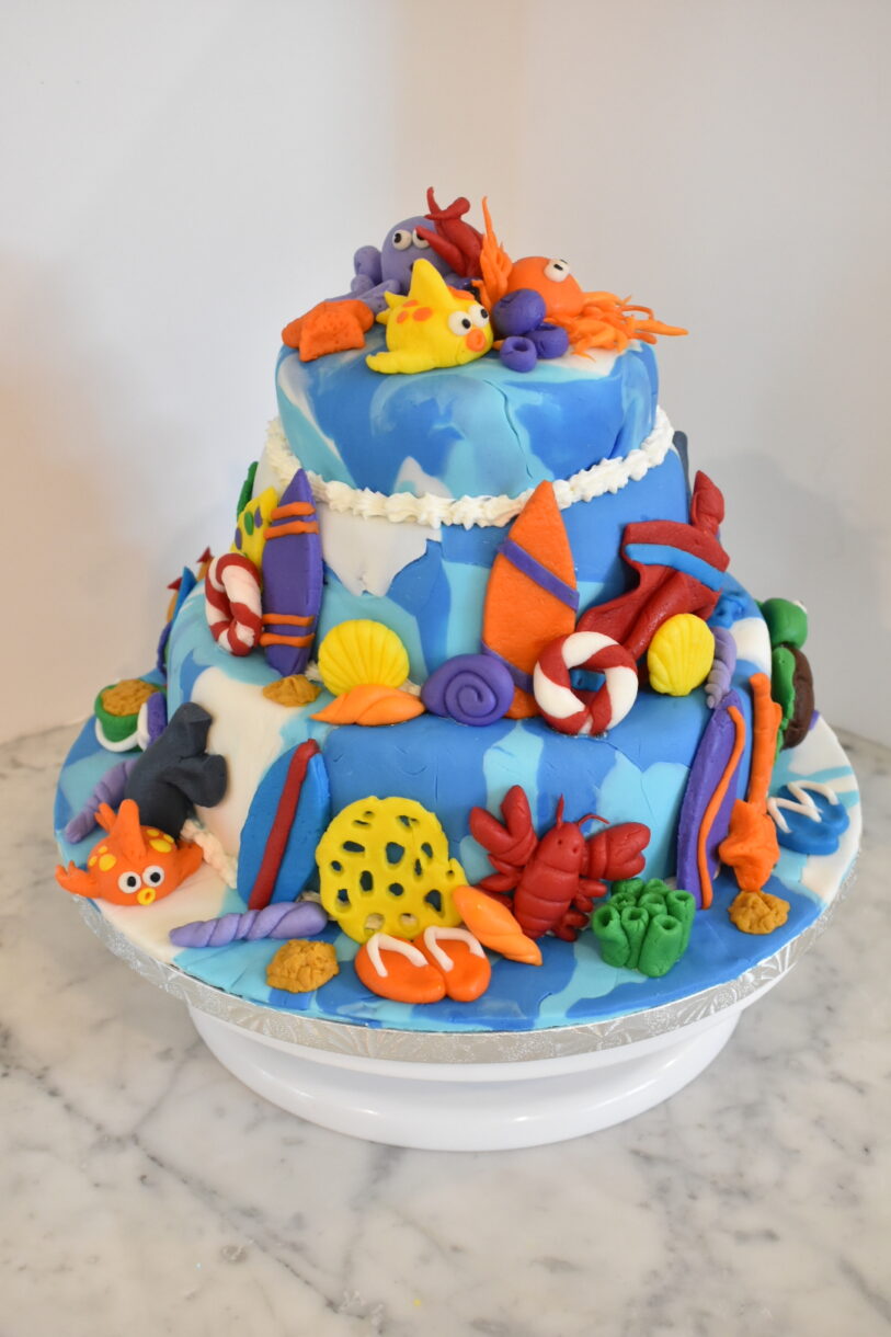 Beach themed cake on a cake stand, sitting on a marble countertop