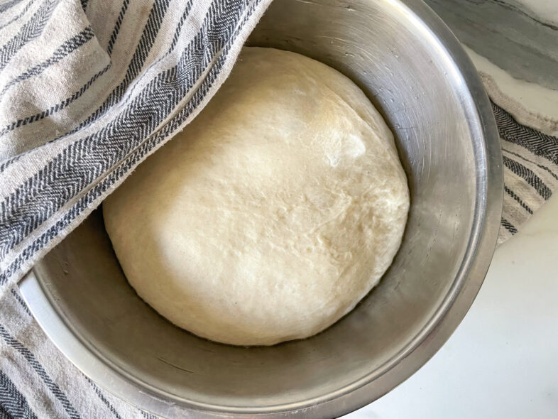 Pizza dough in metal bowl on marble counter