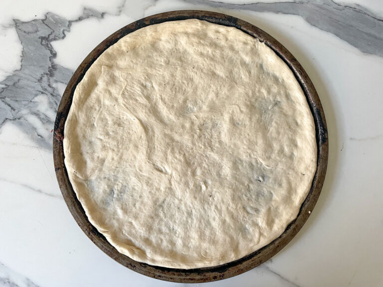 Pizza dough in pan on marble countertop