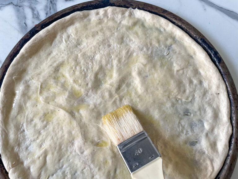 Pastry brush brushing oil on unbaked pizza crust