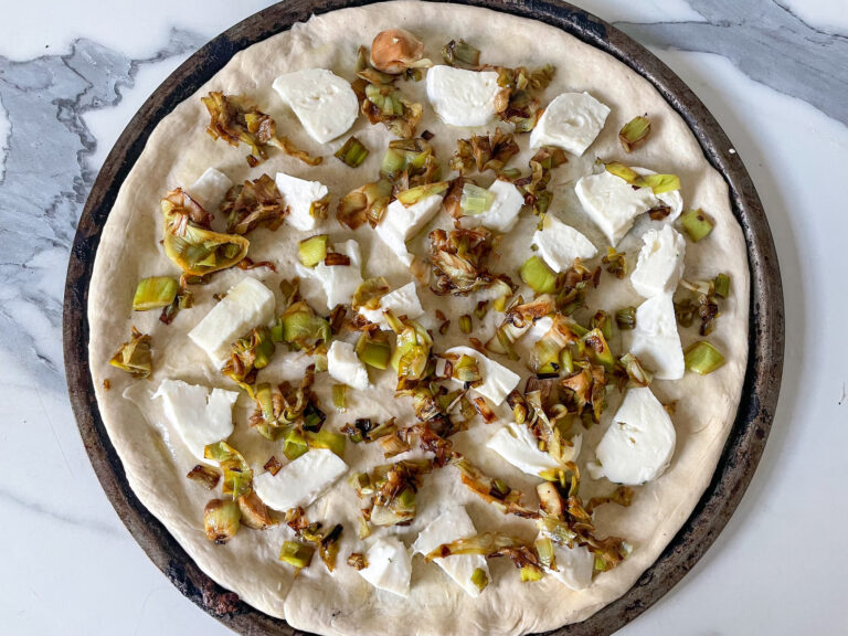 Unbaked pizza crust with cheese and leeks