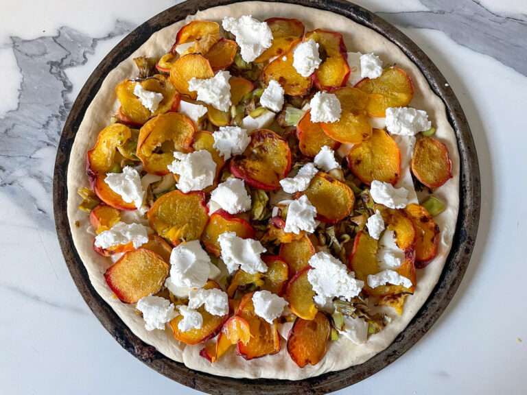 Peach and goat cheese pizza on marble countertop, before baking